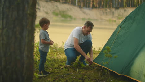 Little-boy-helps-his-father-set-up-a-tent-on-the-shore-of-the-lake-in-the-woods